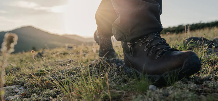 The brown leather Oboz Yellowstone boot close up while hiking through a vast mountainous landscape.